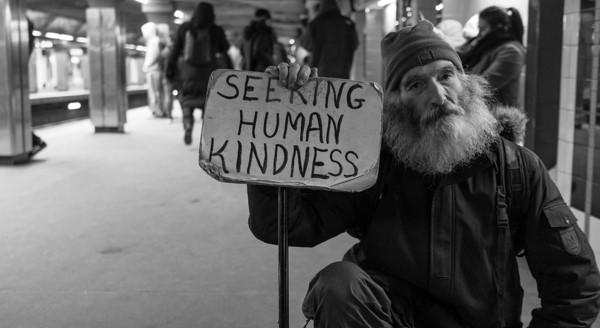 portrait in black and white of a man holding a sign that says "seeking human kindness"